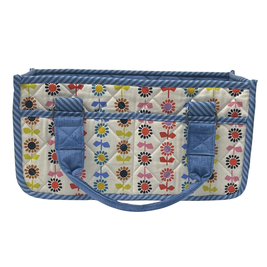 A quilted fabric organizer bag with a colorful floral and bow pattern on a cream background, framed by blue striped borders and solid blue handles, shown against a plain white background.