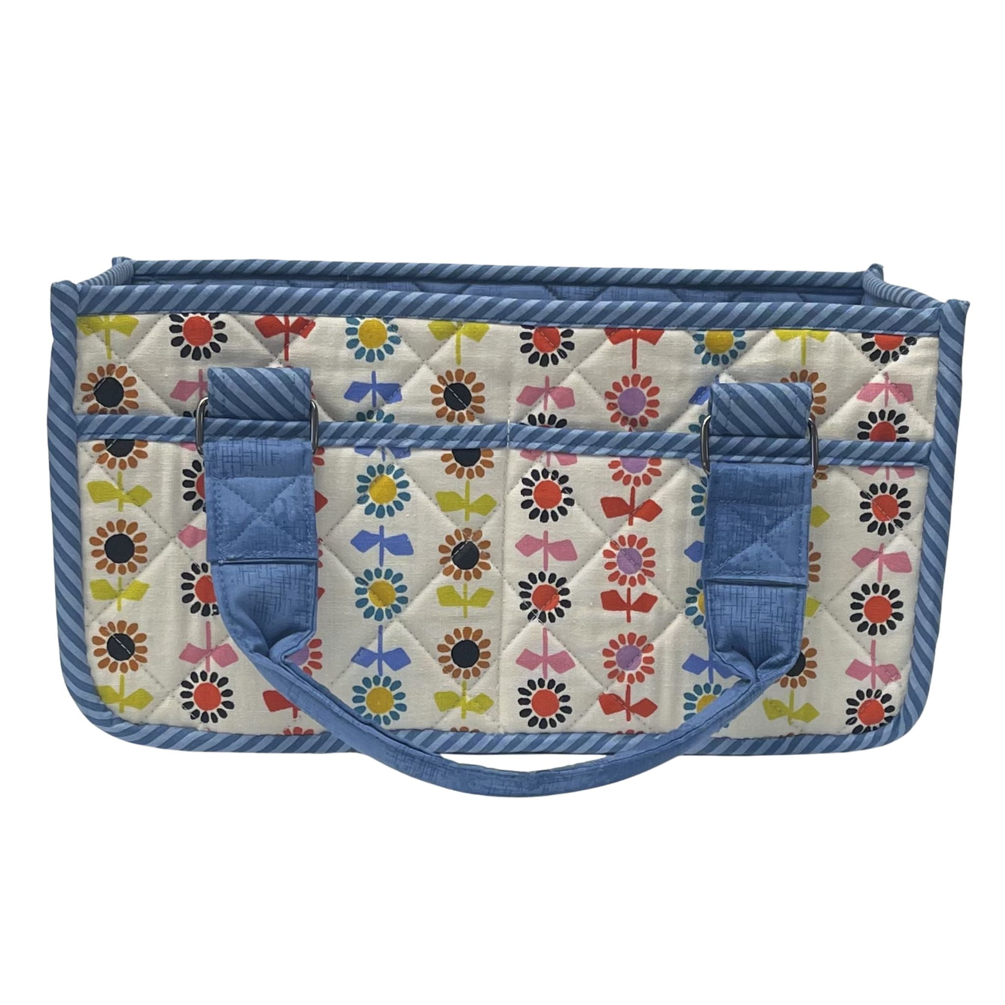 A quilted fabric organizer bag with a colorful floral and bow pattern on a cream background, framed by blue striped borders and solid blue handles, shown against a plain white background.