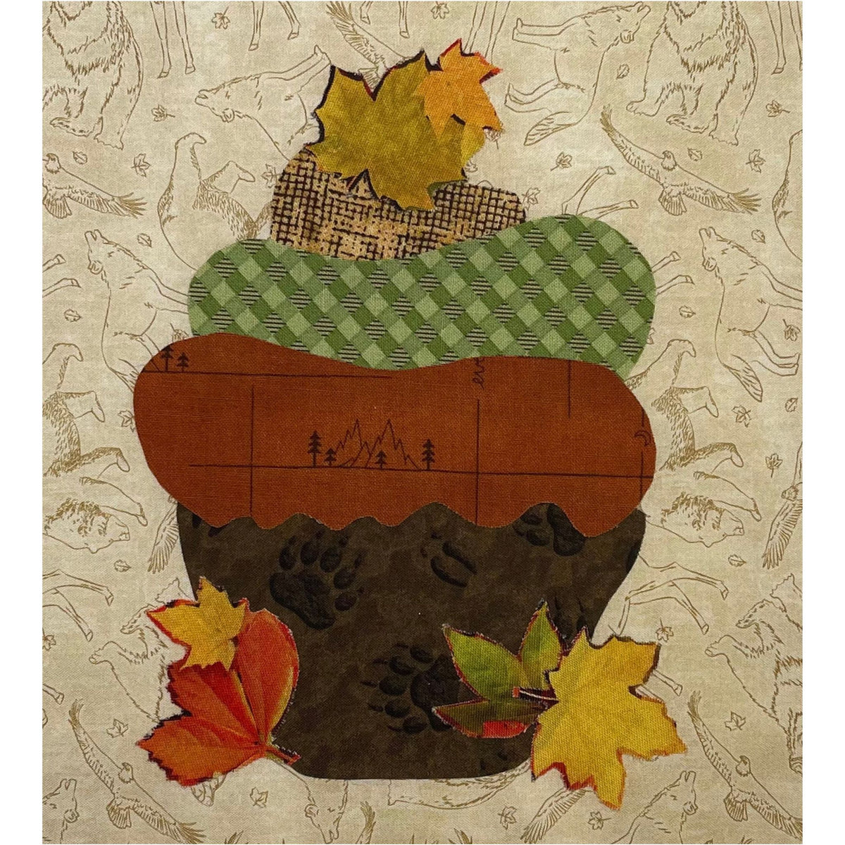 A square art print or textile panel featuring a stylized acorn made from layered autumn-themed fabrics and paper. The acorn has a brown earth-like base with dark brown paw-print texture, a medium brown section with mountain line art, a green diamond-patterned upper section, and yellow/orange leaf accents.