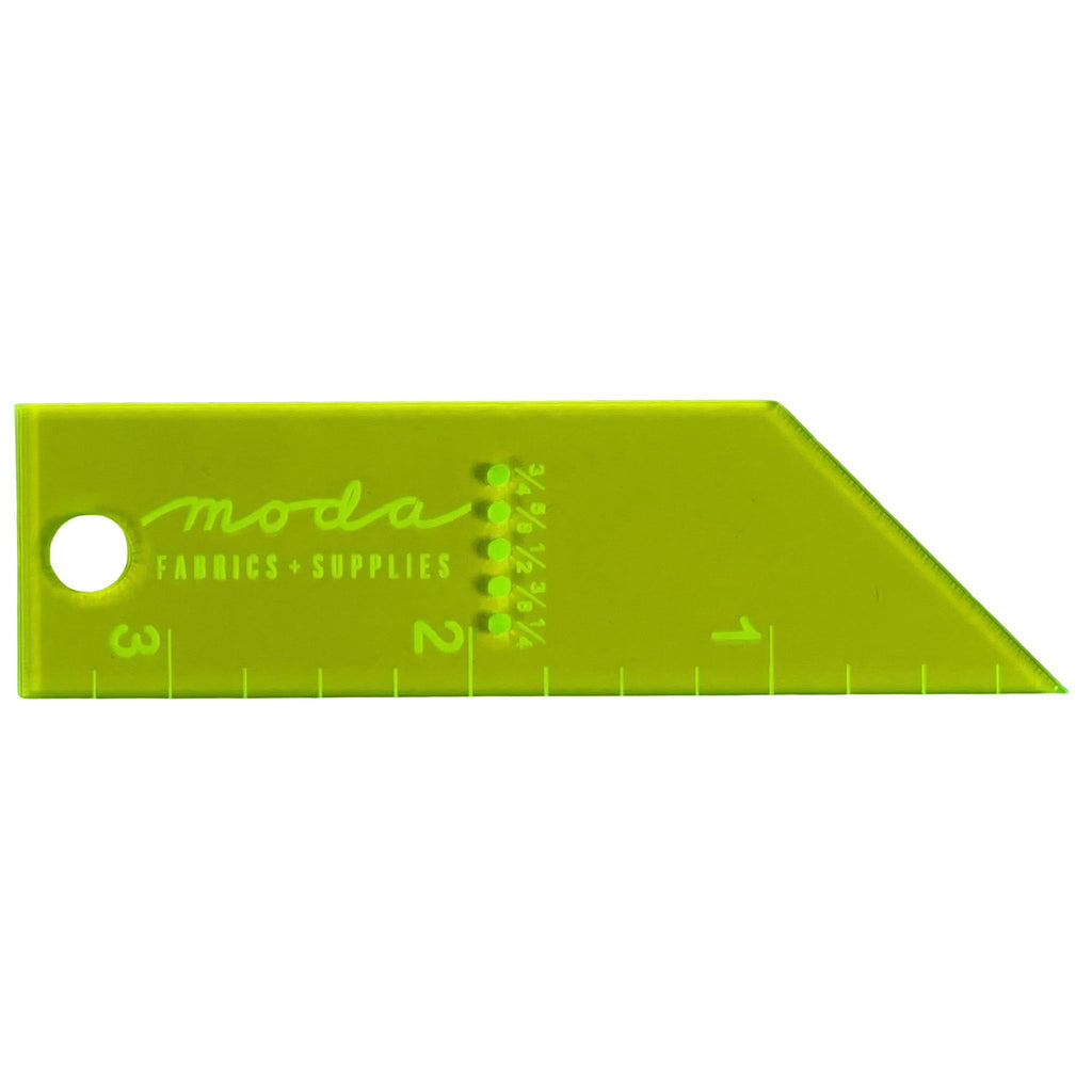 A lime green Moda Fabrics Supplies triangular ruler with measurement markings in inches and centimeters, featuring a circular hole on the left side.