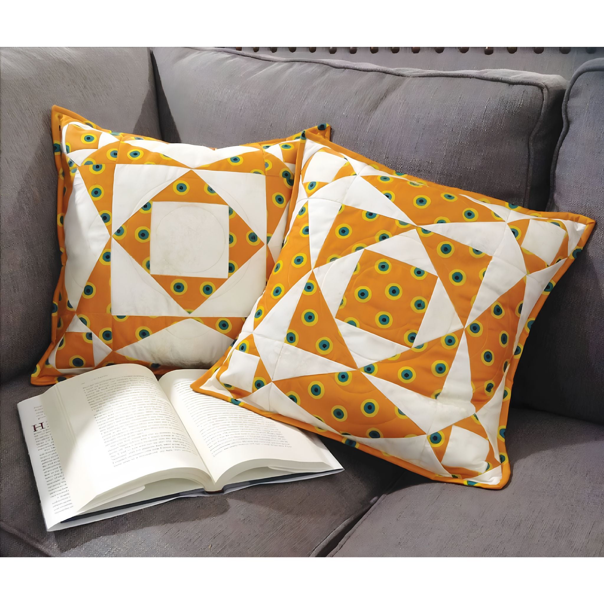 Two decorative pillows with geometric patterns on a gray couch next to an open book.